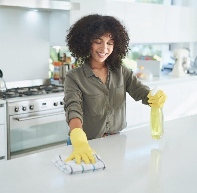 Mujer limpiando un paño de microfibra y un limpiador multiusos en la encimera de la cocina