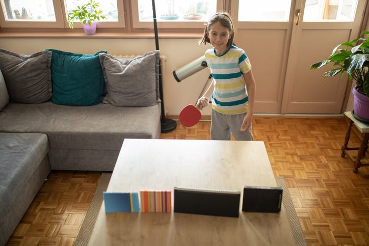 Un niño juega al ping-pong en una sala con piso de madera.