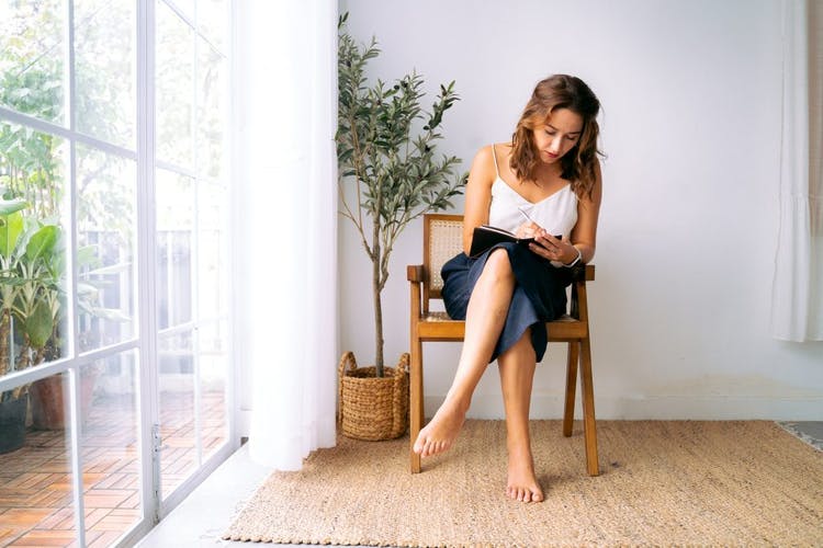 Mujer tomando notas sentada en una silla que está sobre una alfombra de sisal en tonos marrones.