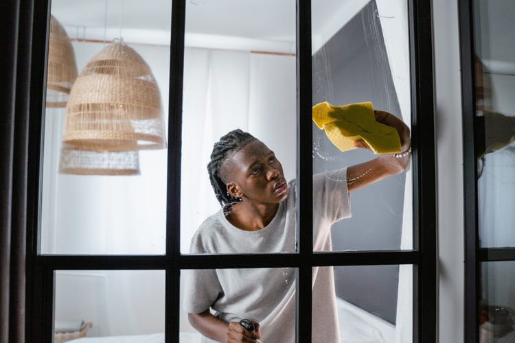 Un hombre negro está limpiando una ventana de vidrio en su casa con un paño amarillo.