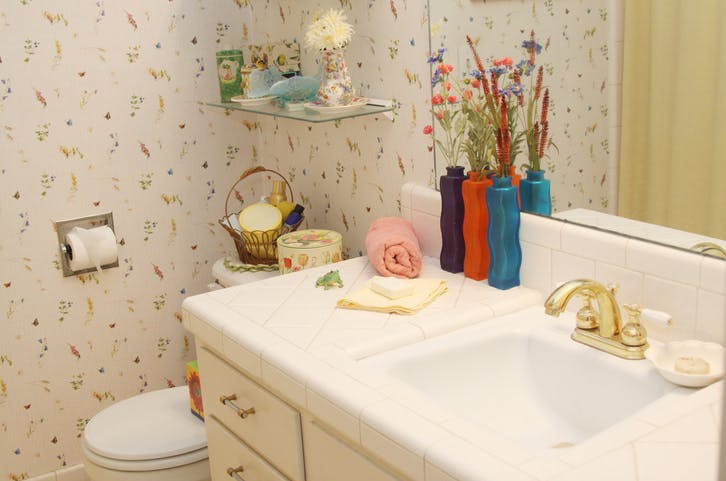 Un baño con papel pintado estampado.  El inodoro es blanco y tiene un grifo dorado.  La iluminación es cálida.
