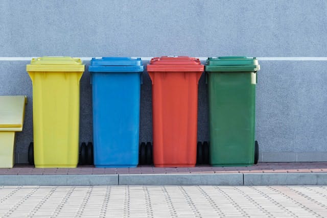 Los coloridos contenedores de recolección reciclable se encuentran en un ambiente al aire libre.