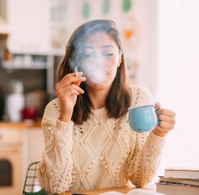 Mujer sentada en la mesa fuma y bebe café.