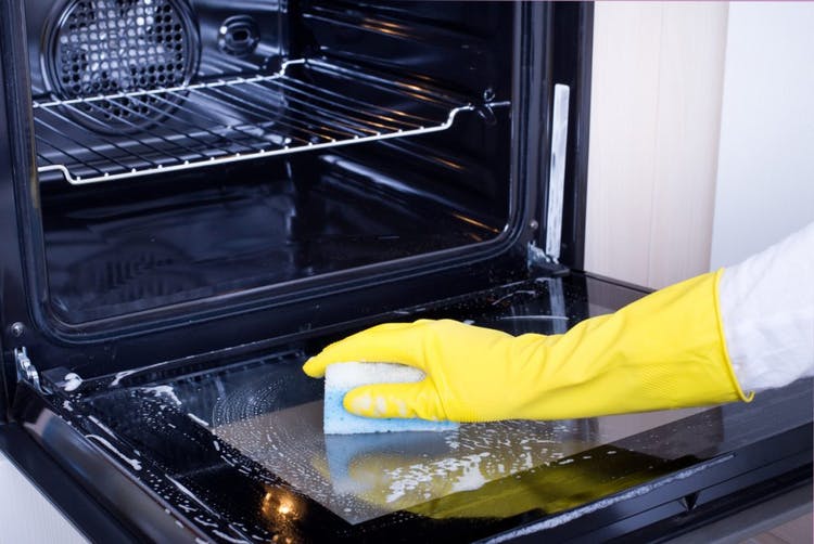 La mujer usa un guante de limpieza amarillo para limpiar la puerta del horno