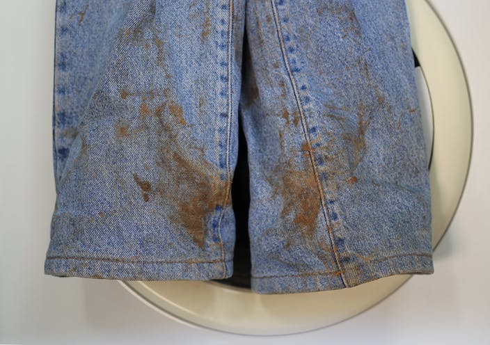 Un par de jeans manchados de barro frente a una lavadora.