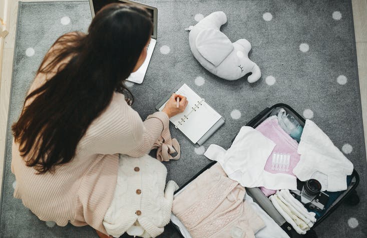 Una mujer embarazada tomando notas y clasificando su bolsa de maternidad.