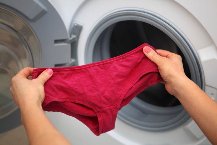 Mujer sosteniendo bragas rojas en sus manos frente a una lavadora.  Concepto para lavar bragas.