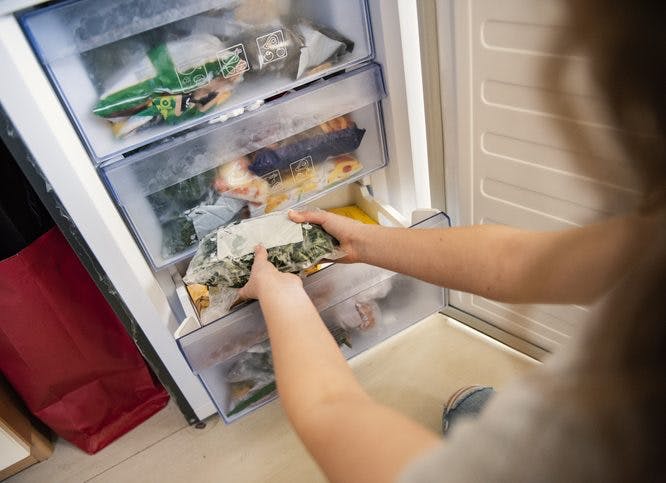 Una mujer está organizando comidas en su congelador.
