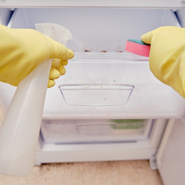 Una persona que limpia un congelador sucio con guantes de limpieza y un estropajo.