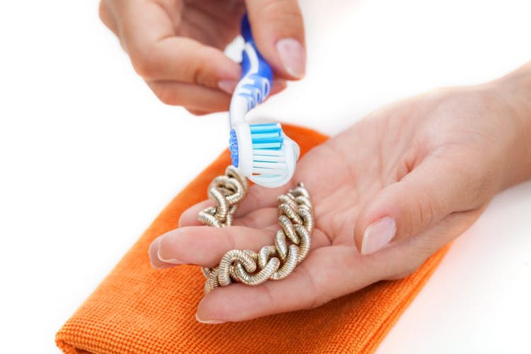 Mujer limpia una pulsera con pasta de dientes y cepillo de dientes
