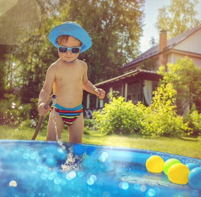 Niño llenando una piscina de plástico con una manguera en un día soleado