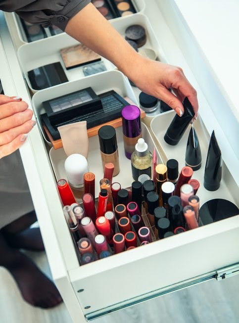 Una mujer está organizando una serie de maquillajes dentro de un gran cajón de la cómoda.