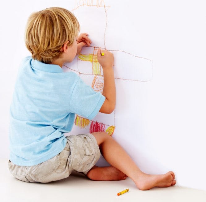 Niño hace dibujos con lápices de colores en la pared