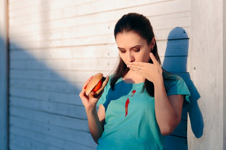 Una mujer está comiendo una hamburguesa y le cae salsa en la ropa.