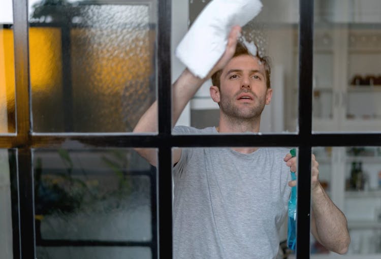 El hombre usa un producto de limpieza y un paño para limpiar el vidrio de la ventana de aluminio en casa.