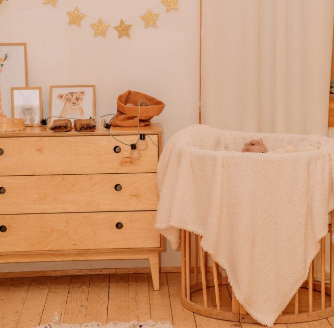 Una habitación de bebé.  Es posible ver una cómoda y una cuna.  La iluminación tiene un tono cálido y el suelo es de madera.  La habitación es sencilla y tiene pocos detalles.