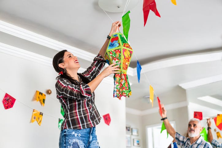 Una mujer está colocando globos de Festa Junina en el techo.