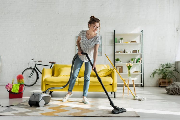 mujer limpiando la alfombra en casa usando una aspiradora