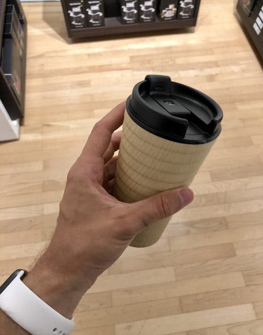Un hombre está en la oficina con su taza termo de café recién hecho.