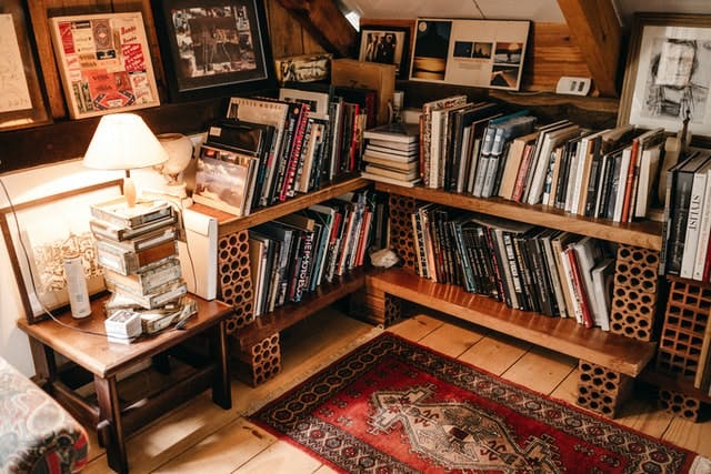 Una sala de estar de estilo vintage llena de libros.  La librería está hecha de tablones de madera brillantes sostenidos por bloques de construcción de color naranja.