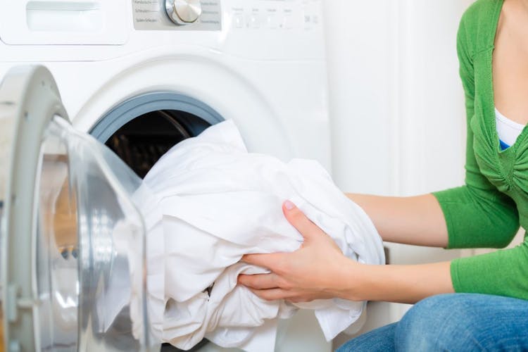 Mujer pone ropa blanca para lavar en la lavadora