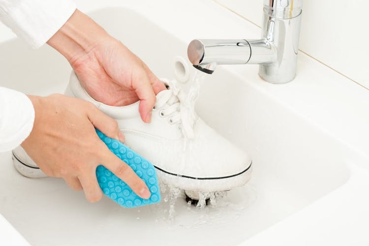 Persona lavando zapatillas blancas con agua y un cepillo azul.
