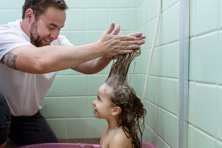 Un padre baña a su hija y le enjabona el pelo.