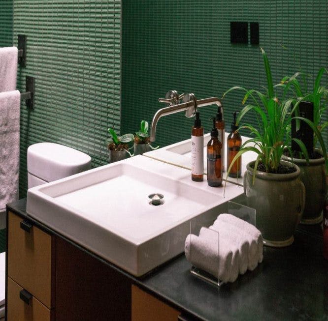 Un baño con azulejos con tonos verdes.  Hay lámparas colgantes sobre el inodoro y la habitación tiene un ambiente elegante.