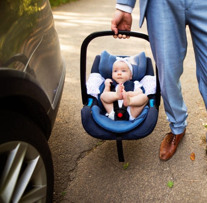 Un hombre vestido de vestido acaba de sacar a su hijo del coche.  El niño se acomoda en la mochila porta bebé.