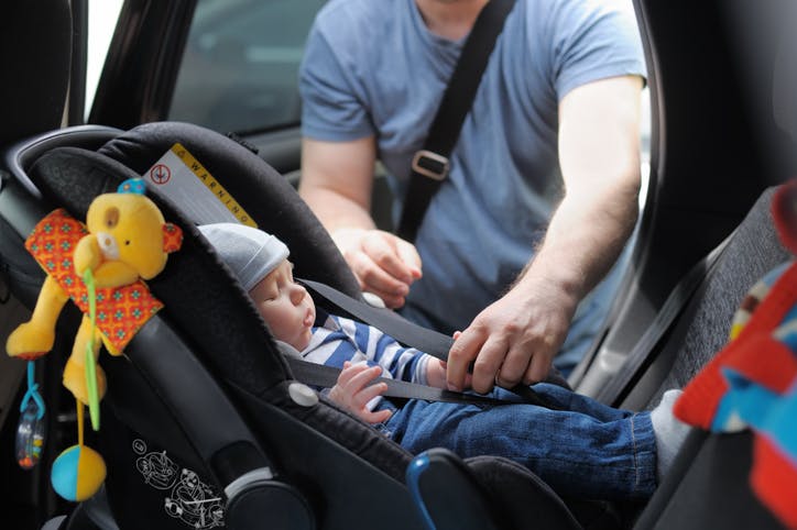 Un hombre está guardando a su hijo en el asiento de bebé en el coche.
