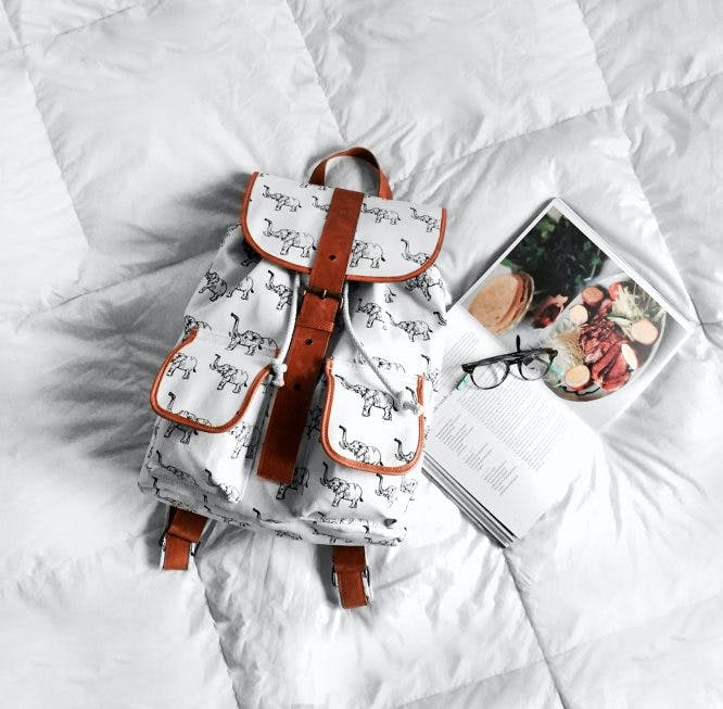 Mochila blanca sobre una cama con sábanas blancas.