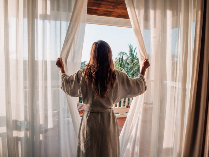 Una mujer abre las cortinas de su casa por la mañana justo después de despertarse.