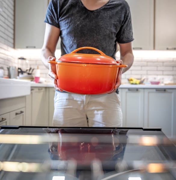Un hombre sostiene una vasija de cerámica de color naranja.  Está en tu cocina.