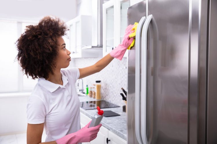 Mujer limpia el exterior del refrigerador de acero inoxidable