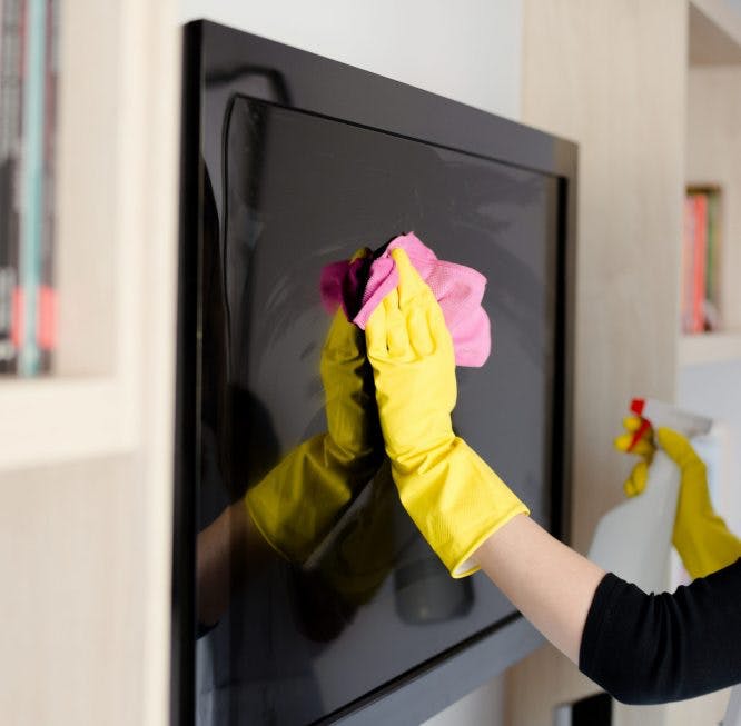 Mujer usa guantes amarillos y un paño rosa para limpiar la pantalla de su televisor