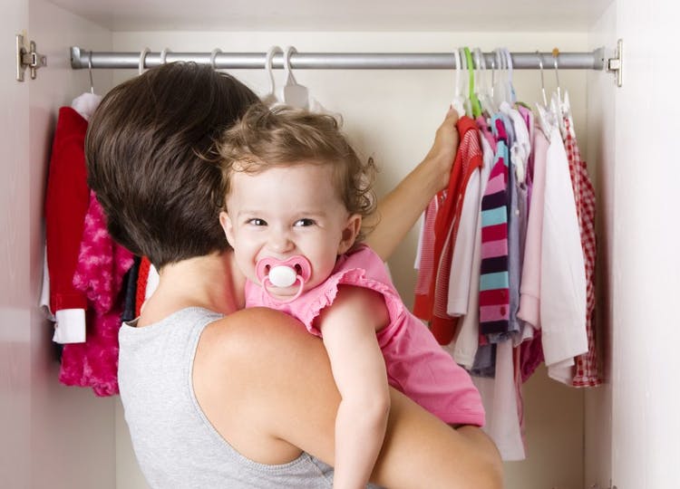 Madre con hija en su regazo arregla la ropa en el guardarropa del bebé