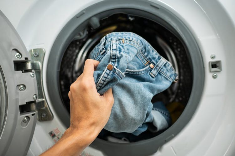 persona poniendo jeans en la lavadora
