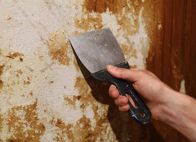 Un hombre raspa la pared con una espátula de metal resistente.