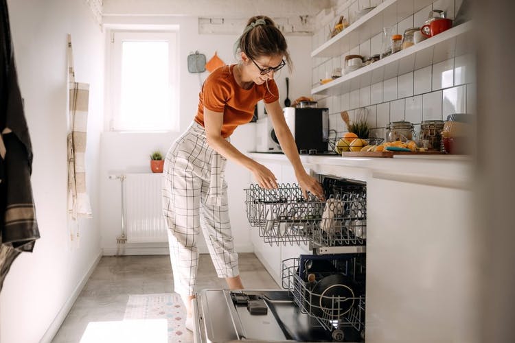 Una mujer está metiendo platos en un lavavajillas.