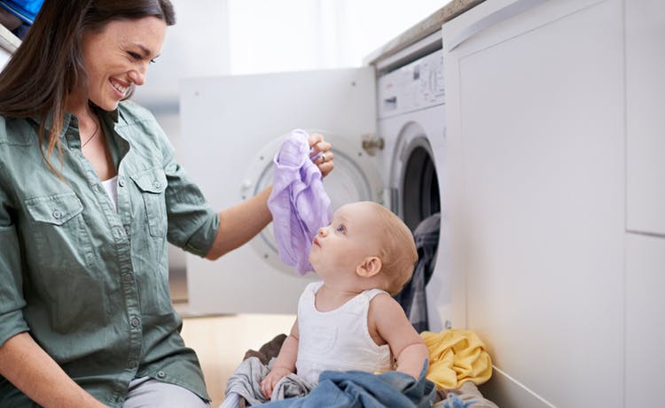 Una mujer está con su hija al lado de la lavadora.  Separa la ropa del niño para lavarla.