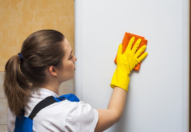 la mujer limpia la pared con un paño y un guante de limpieza
