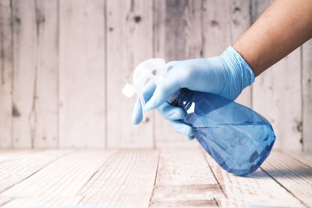 Una persona que usa guantes está rociando desinfectante de una botella de spray sobre un piso de madera. 