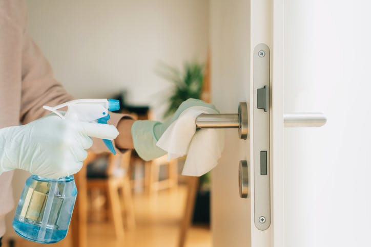 Una persona limpia la manija de una puerta de PVC.  Ella usa un paño y guantes.