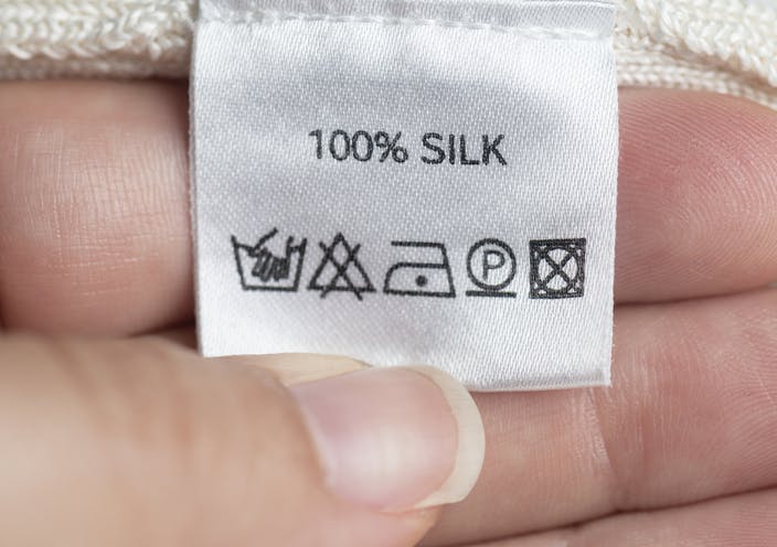 Una mujer sostiene una etiqueta de ropa con la inscripción: 100% seda y símbolos de lavado.