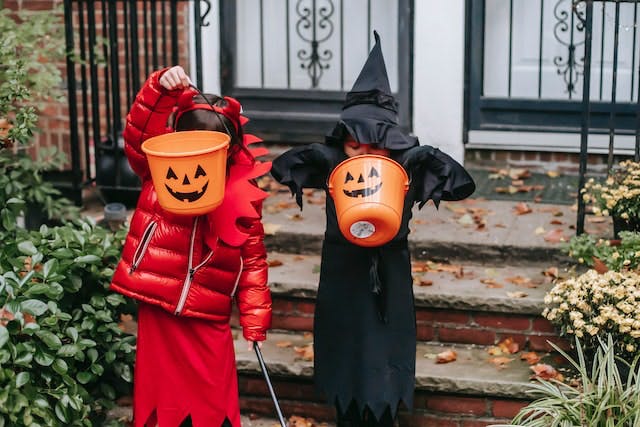Dos niños disfrazados de Halloween.  Están en el área exterior de una casa y sostienen baldes para pedir dulces.