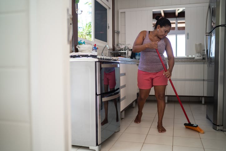 mujer barre el piso de la cocina